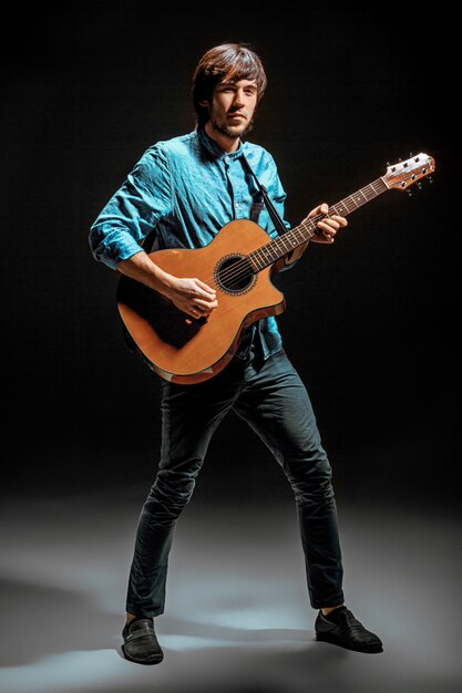 Cool guy debout avec guitare sur mur sombre