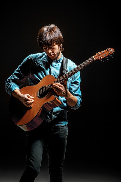 Cool guy debout avec guitare sur mur sombre