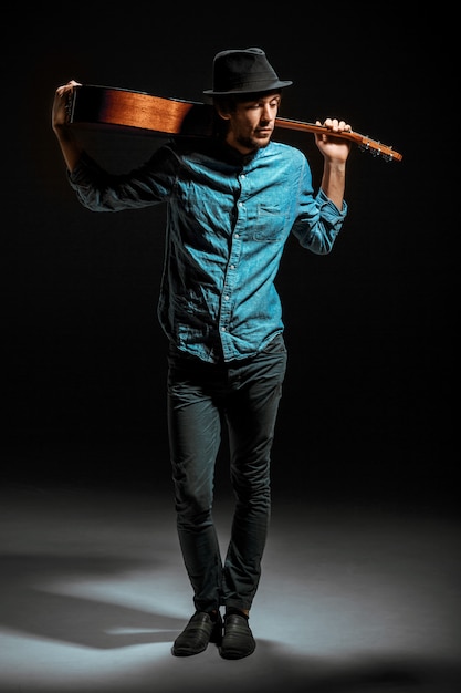 Photo gratuite cool guy debout avec guitare sur mur sombre