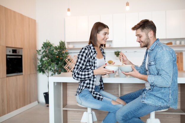 Cool jeune homme et femme heureux dans la cuisine prenant le petit déjeuner, couple ensemble le matin, souriant, parlant