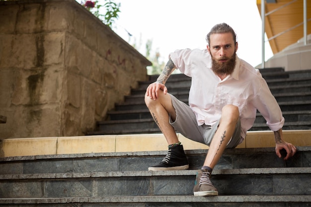 Cool mec tatoué et barbu posant en plein air dans la ville