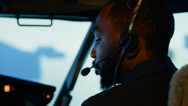 Copilote afro-américain se préparant à décoller et à voler, en utilisant la commande du tableau de bord dans le cockpit. Navigation sur le pare-brise et boutons du panneau de commande pour voyager avec l'avion. Fermer.