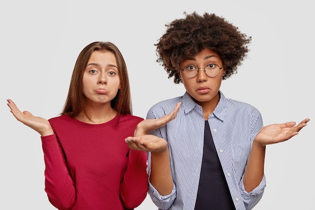 Photo gratuite copines désemparées posant contre le mur blanc