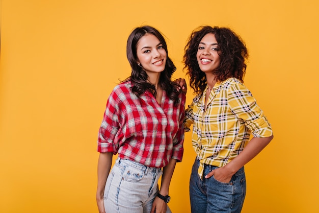 Les copines portent des chemises similaires pour être mignonnes lors d'une séance photo. Portrait de brune joyeuse aux yeux bruns.