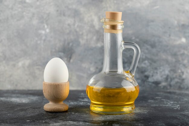 Un coquetier en bois avec un œuf de poule bouilli et une bouteille en verre d'huile.