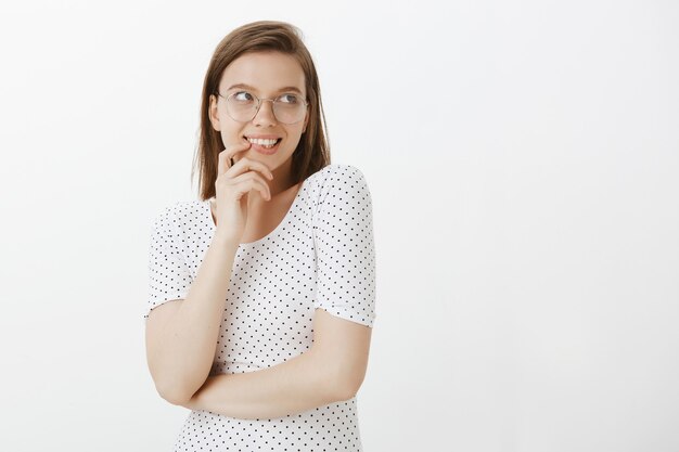 Coquettish femme idiote à lunettes souriant, rougissant et regardant directement votre logo