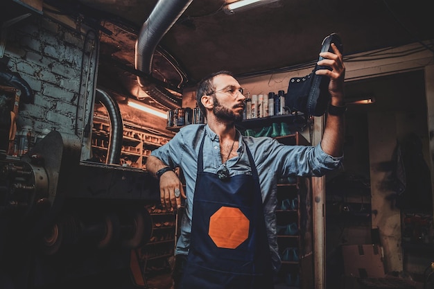 Le Cordonnier Barbu à Lunettes Regarde La Botte Tout En La Tenant à La Main.