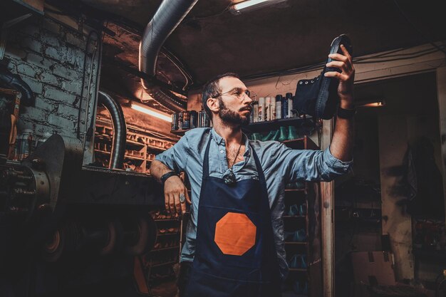 Le cordonnier barbu à lunettes regarde la botte tout en la tenant à la main.