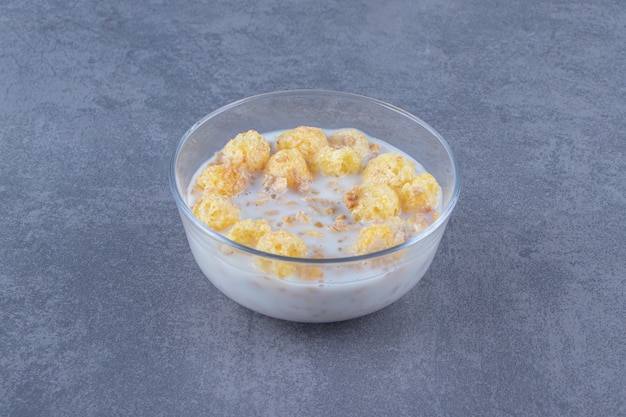 Cornflakes au lait dans un bol en verre, sur fond bleu.