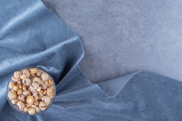 Cornflakes dans un bol en verre sur un morceau de tissu, sur le fond de marbre.