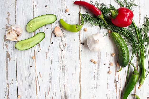 Cornichons sur table en bois blanc avec poivrons verts et rouges, fenouil, sel, grains de poivre noirs, ail, pois, gros plan, concept santé, vue de dessus, vue à plat