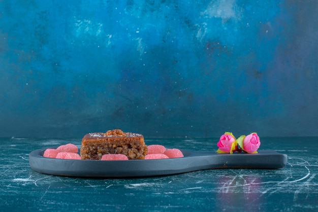 Photo gratuite corolles de fleurs à côté de marmelades autour d'une tranche de bakhlava sur un petit plat de service sur fond bleu. photo de haute qualité