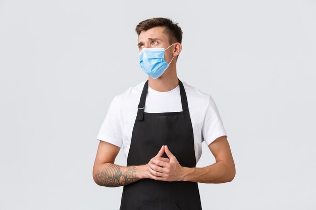 Coronavirus, distanciation sociale dans les cafés et restaurants, affaires pendant le concept de pandémie. Barista déçu et triste, vendeur en tablier et masque médical à gauche mécontent et contrarié