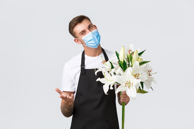 Coronavirus, entreprise de distanciation sociale pendant le concept de pandémie de covid-19. Vendeur charmant, fleuriste dans un magasin de fleurs faisant un bouquet de lys blancs pour le client, portant un masque médical