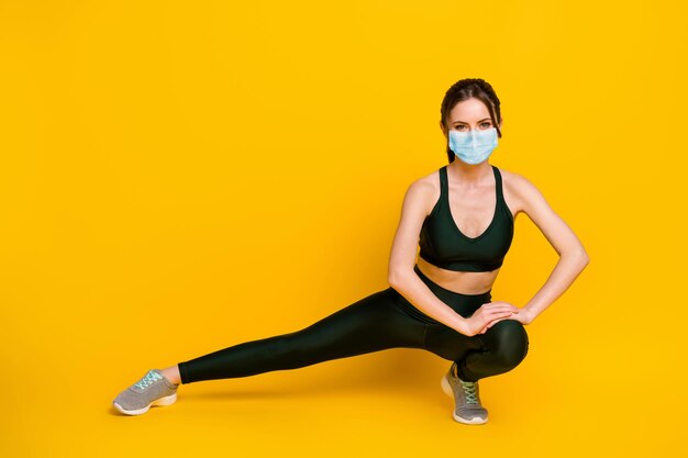 Corps de pleine longueur de joyeuse fille forte faisant de l'exercice physique porter un masque isolé sur fond de couleur jaune vif