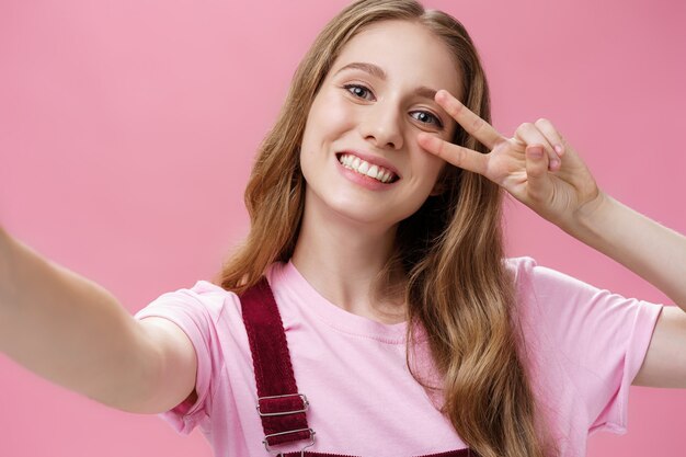 Corps positif, cicatrices et concept de positivité de la peau. Portrait d'une charmante jeune fille insouciante avec une blessure au bras tirant les mains vers pour saisir la caméra et prendre un selfie faisant un signe de paix avec un large sourire.