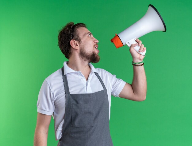 À côté d'un jeune coiffeur masculin en uniforme, parle sur un haut-parleur isolé sur un mur vert