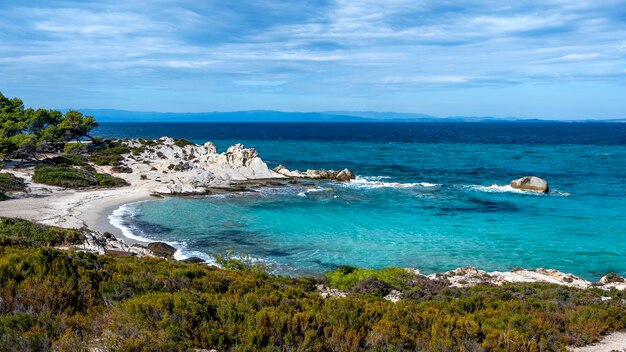 Côte de la mer Égée avec verdure autour, rochers, buissons et arbres, eau bleue avec des vagues, Grèce