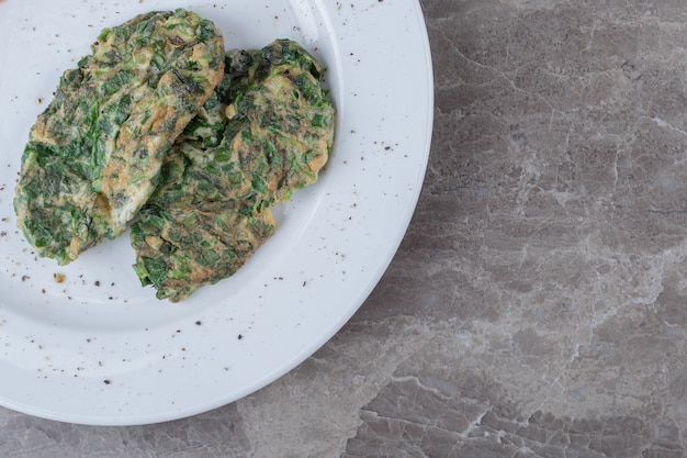 Côtelette d'oeufs avec des verts sur une plaque blanche.