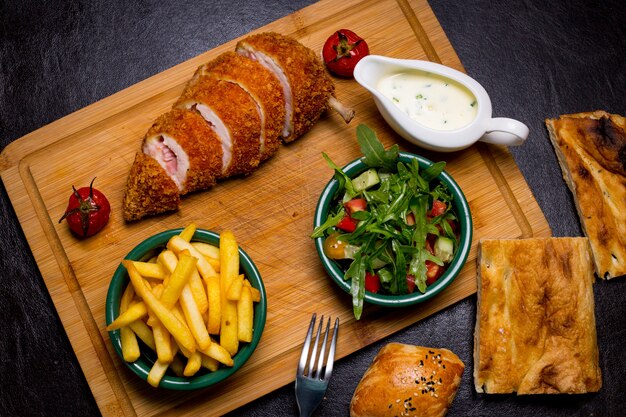 Côtelette de style de Kiev sur la planche de bois avec des frites roquette sauce tomate concombre vue de dessus