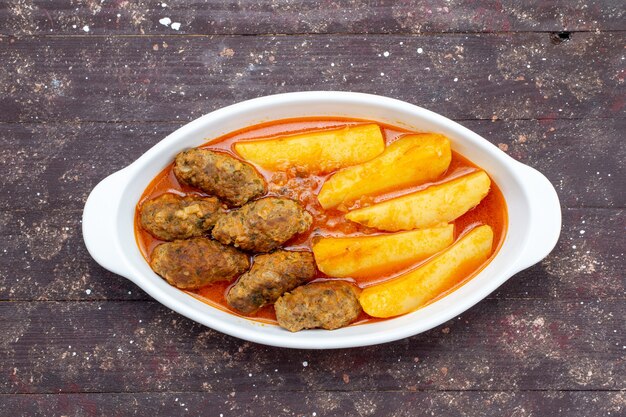 Côtelettes de viande savoureuses cuites avec pommes de terre et sauce à l'intérieur de la plaque sur brun