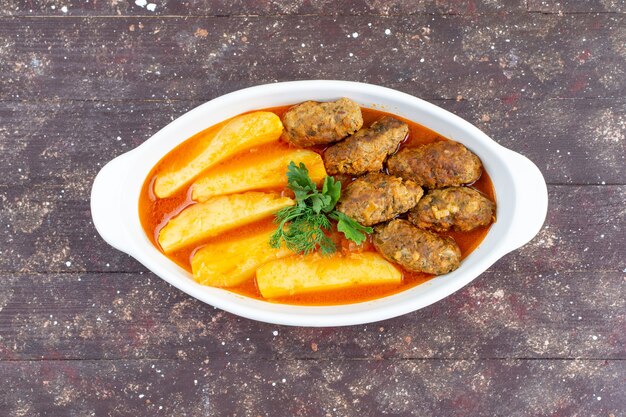 Côtelettes de viande savoureuses cuites avec pommes de terre et sauce à l'intérieur de la plaque avec des verts sur brun