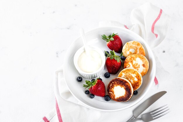 Cottage fromage crêpes crêpes ricotta fritters avec des fraises fraîches et des bleuets d'une assiette de céramique blanche petit déjeuner sain et délicieux pour les vacances