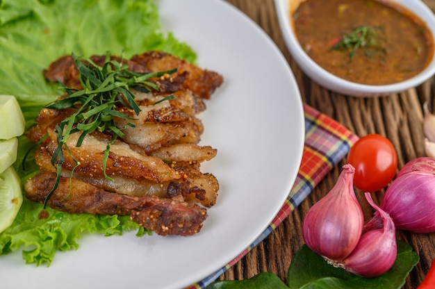 Cou de porc grillé sur une plaque blanche avec oignon rouge, tomate et piment sur la table en bois.