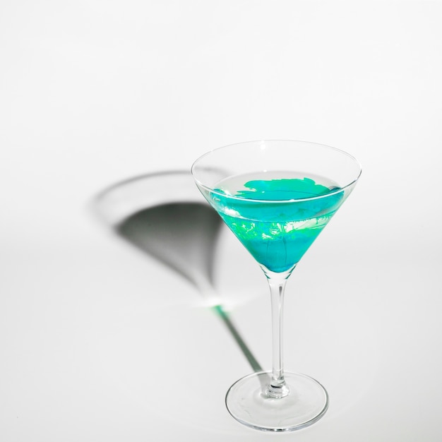 Couleur turquoise diffuse dans l&#39;eau à l&#39;intérieur d&#39;un verre à martini avec ombre sur fond blanc