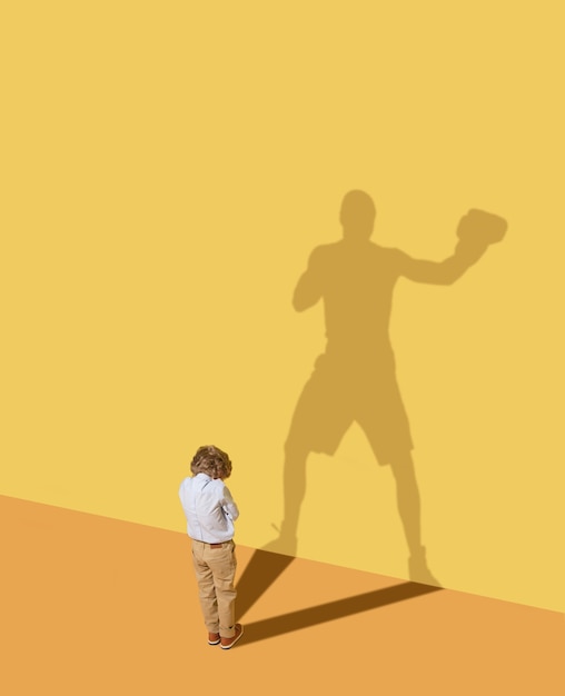 Le coup du roi pour gagner. Futur champion. Concept d'enfance et de rêve. Image conceptuelle avec enfant et ombre sur le mur jaune du studio. Le petit garçon veut devenir boxeur et se bâtir une carrière sportive.