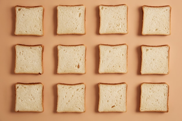 Photo gratuite coup de frais généraux de tranches de pain non torréfiées disposées en rangées, prêt pour le grillage, isolé sur fond de studio beige. préparer un délicieux sandwich. délicieuse collation. produit de boulangerie tranché. mise à plat.