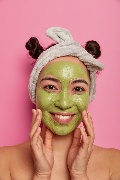 coup de jolie femme naturelle touche les joues sourit doucement et applique un masque de beauté sur le visage se soucie du teint et le corps se tient nu à l'intérieur suit les conseils du cosmétologue comment réduire l'acné