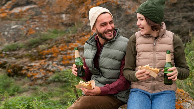 Coup de milieu heureux couple assis sur le rocher boire et manger