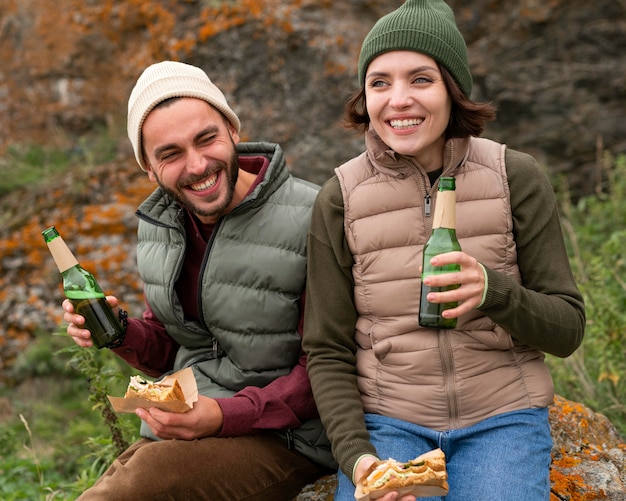 Photo gratuite coup de milieu heureux couple assis sur un rocher et prendre un verre