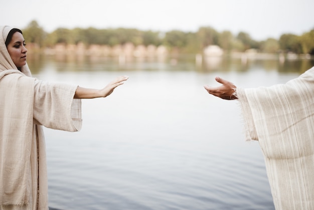 Coup de mise au point peu profonde de femme portant une robe biblique et tendant la main vers la main de Jésus-Christ