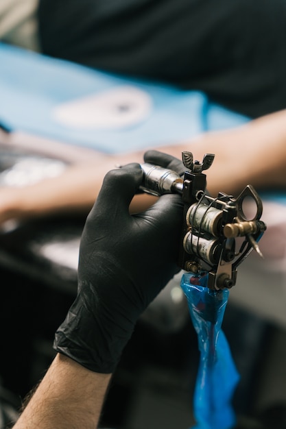 Photo gratuite coup de mise au point sélective de la main d'un tatoueur portant un gant noir et tenant un pistolet de tatouage