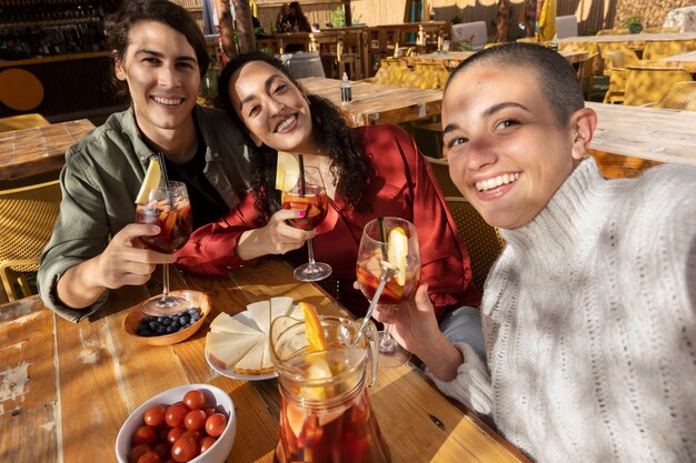 Coup moyen amis heureux prenant selfie avec des boissons