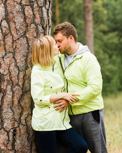 Photo gratuite coup moyen couple s'embrassant à côté d'un arbre