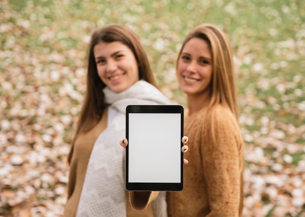 Photo gratuite coup moyen deux femmes souriantes tenant une tablette dans les mains