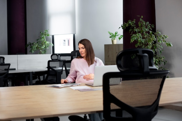 Coup moyen femme assise au bureau avec un ordinateur portable