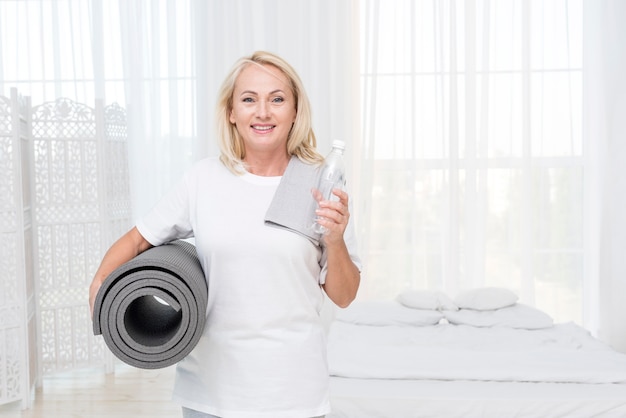 Coup moyen femme heureuse avec de l'eau et un tapis de yoga