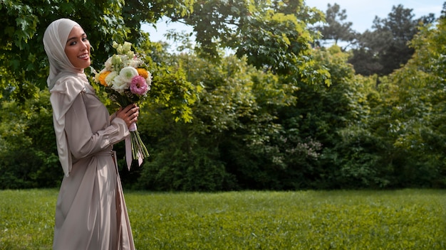 Coup moyen femme musulmane posant avec des fleurs