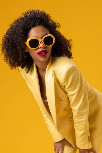 Coup moyen femme posant avec des lunettes de soleil jaunes