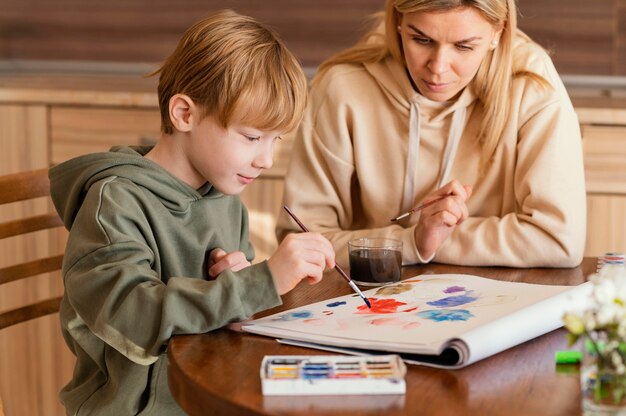 Coup moyen femme regardant enfant peindre