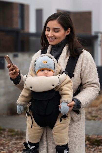 Photo gratuite coup moyen femme tenant bébé dans un porte-bébé