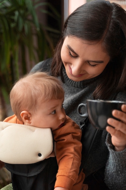 Photo gratuite coup moyen femme tenant bébé dans un porte-bébé