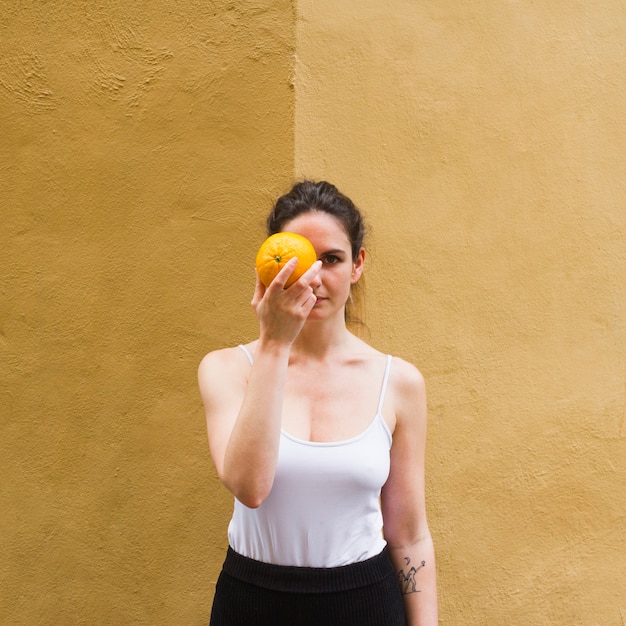 Coup moyen femme tenant une orange qui couvre son oeil