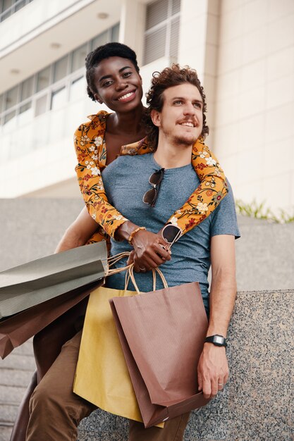 Coup moyen de jeune couple interculturel avec des sacs à provisions posant pour une photo en plein air