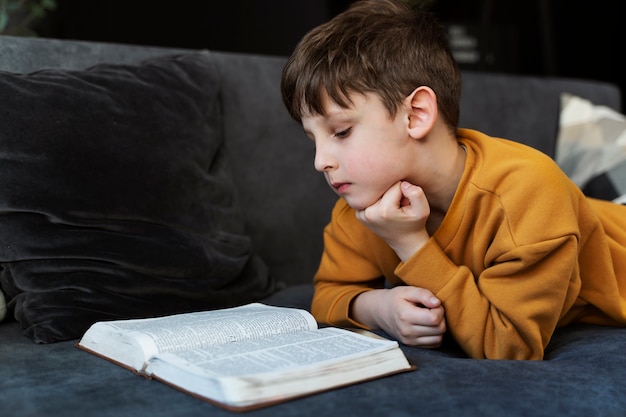 Coup Moyen Petit Garçon Lisant La Bible Sur Le Canapé