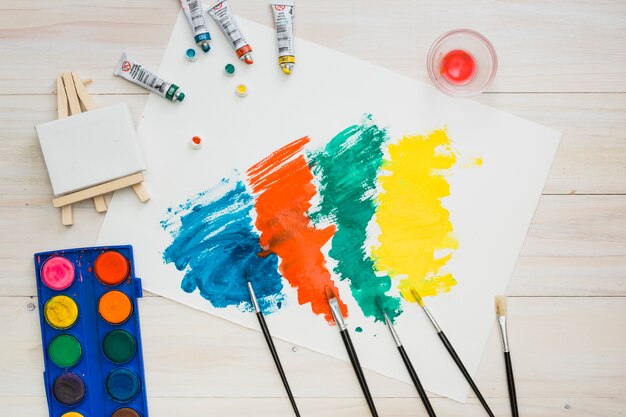 Coup de pinceau multicolore sur une page blanche avec du matériel de peinture sur une table en bois